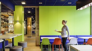 Un café moderne avec un plancher en bois, des murs verts et différents types de sièges, notamment des tables et des chaises.