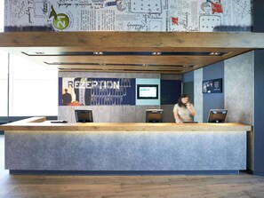 A reception area with a modern design, including a reception desk, a digital screen, and a wall with a 'RECEPTION' sign. - ibis budget Basel City (Basel)