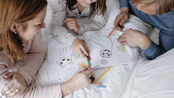Tres personas acostadas en una cama, coloreando una página con diversos patrones y diseños.