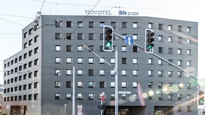A Novotel hotel with a modern design, located at a street intersection with traffic lights and tram tracks.
