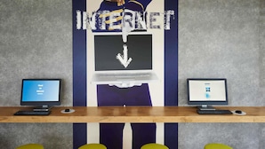 A workspace with two computers, a large 'INTERNET' sign, and three yellow stools. - ibis budget Basel City (Basel)