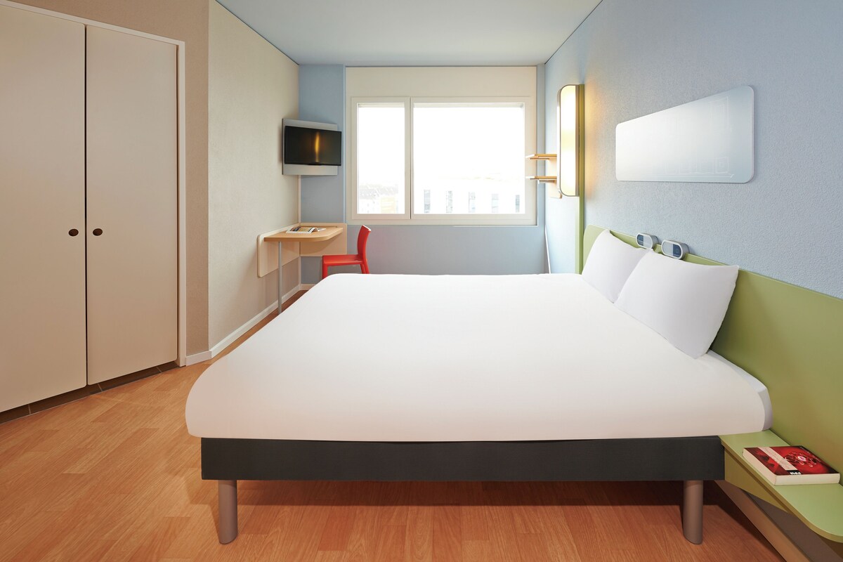 Une chambre d’hôtel avec un lit, un bureau, une chaise, une télévision et une fenêtre.