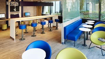 Eine moderne Bar mit Holztresen, mehreren Barhocker und einer Sitzecke mit runden Tischen und bunten Stühlen.