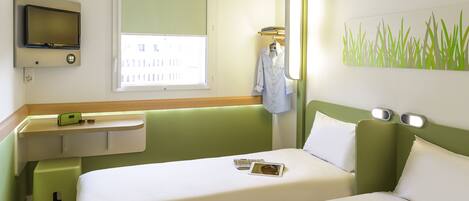 A hotel room with a bed, a TV mounted on the wall, a window with blinds, a bedside table with a phone and glasses, and a wall art piece.