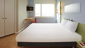 Habitación de hotel con cama, escritorio, silla, televisor y ventana.