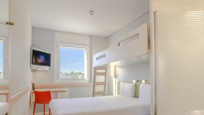 A modern hotel room with a bed, a desk, a chair, a TV, and a window with a city view. - ibis budget Basel City (Basel)
