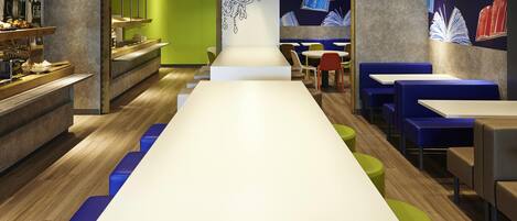 A modern lounge area with a long white table, blue and green seating, and a wall with 'LOUNGE' and book illustrations.