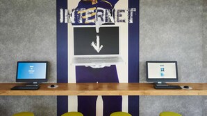 Un espace de travail équipé de deux ordinateurs, d’une grande enseigne indiquant « INTERNET » et de trois tabourets jaunes.