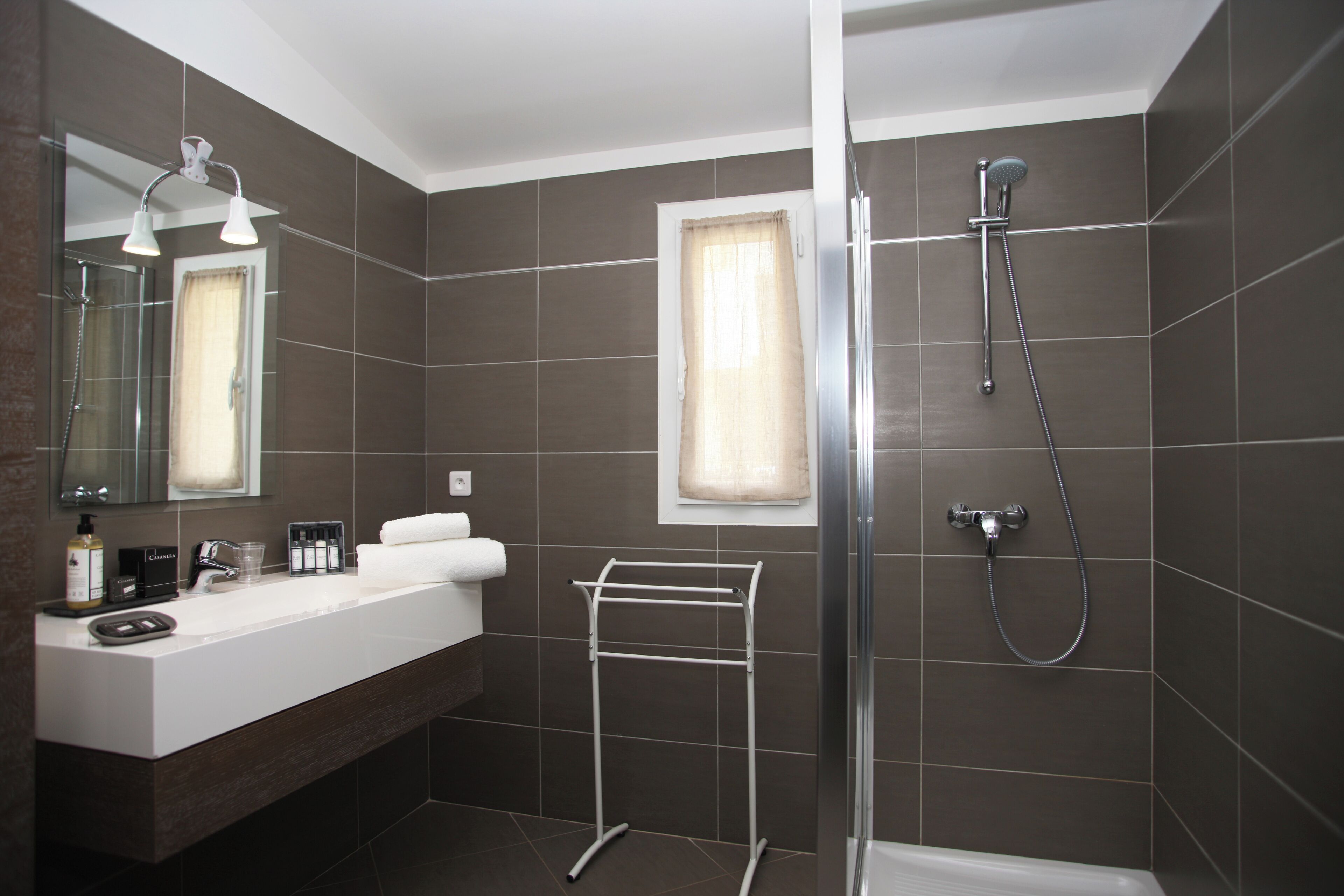 Une salle de bain moderne avec un grand miroir, un lavabo blanc, une douche en verre et un porte-serviettes.