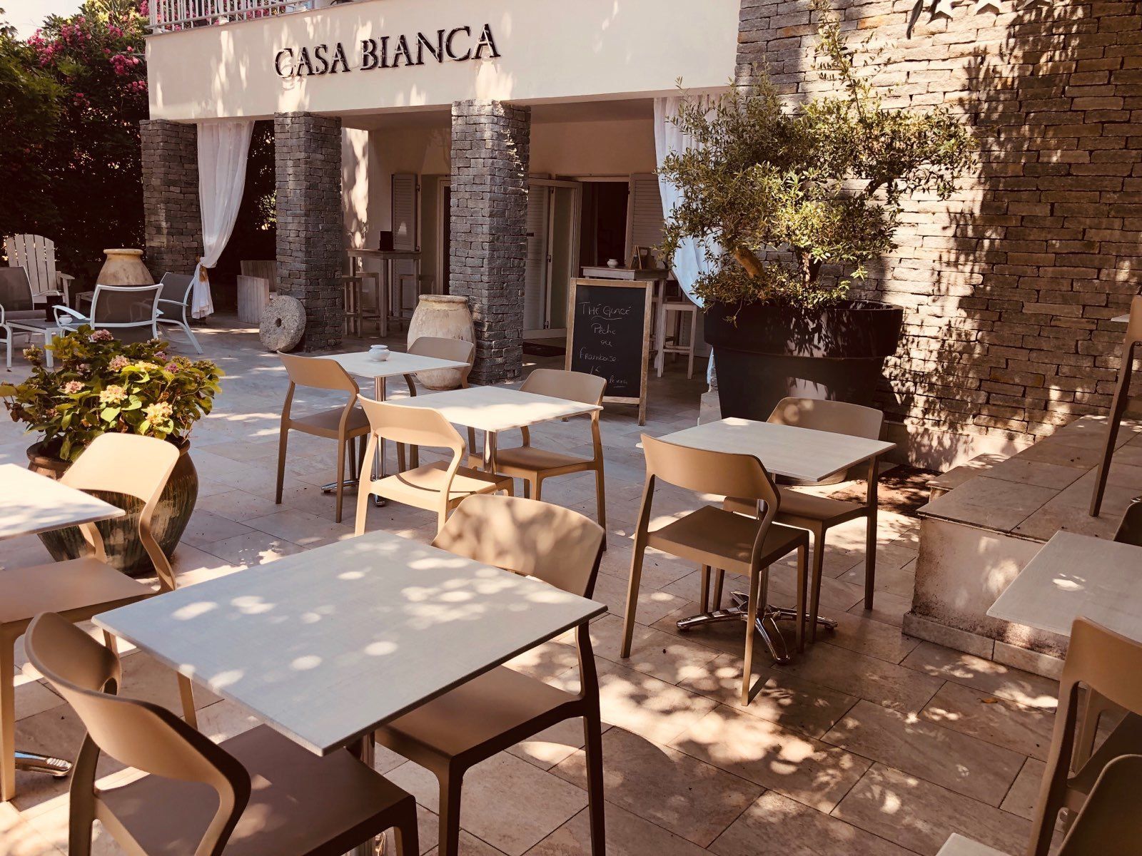 An outdoor seating area with tables and chairs, a stone wall, and a sign reading "CASA BIANCA".