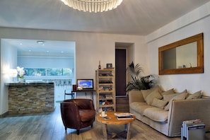 A modern living room with a stone backsplash, a leather chair, a wooden coffee table, a beige sofa, a bookshelf, and a large mirror. - Best Western Hotel Casa Bianca, Piscine Intérieure et Extérieure (Calvi)