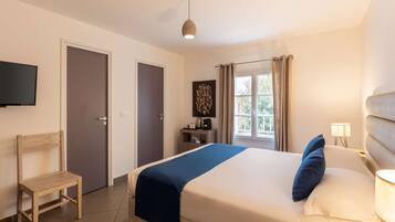Una habitación de hotel con una cama, una silla, un escritorio con lámpara, televisión y una ventana con cortinas.