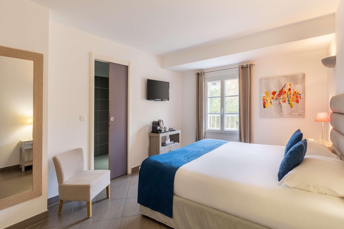 A hotel room with a bed, a chair, a desk, a TV, and a window with curtains.