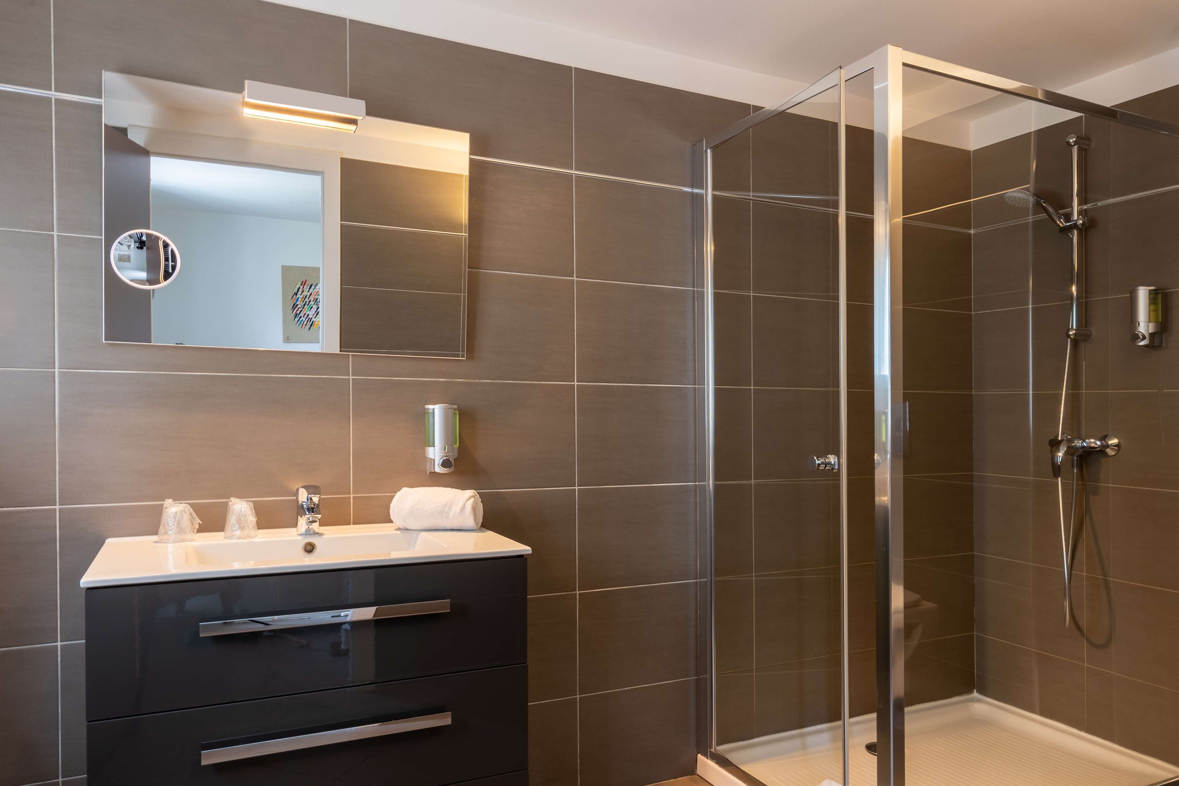 Une salle de bain moderne avec une douche à parois de verre, un meuble-lavabo avec un miroir et un distributeur de savon fixé au mur.