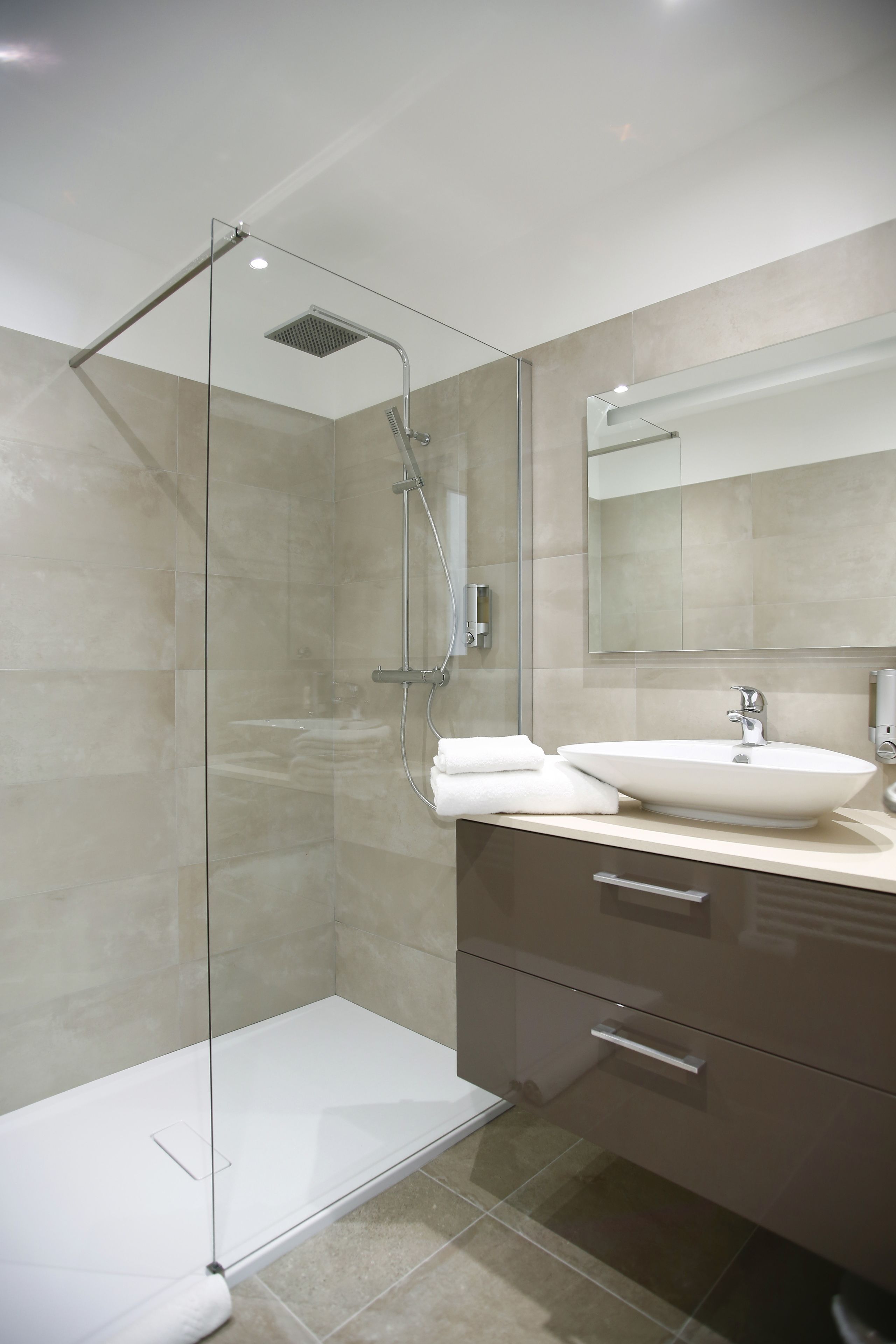 Une salle de bain moderne avec une douche à parois de verre, un lavabo blanc et un grand miroir.