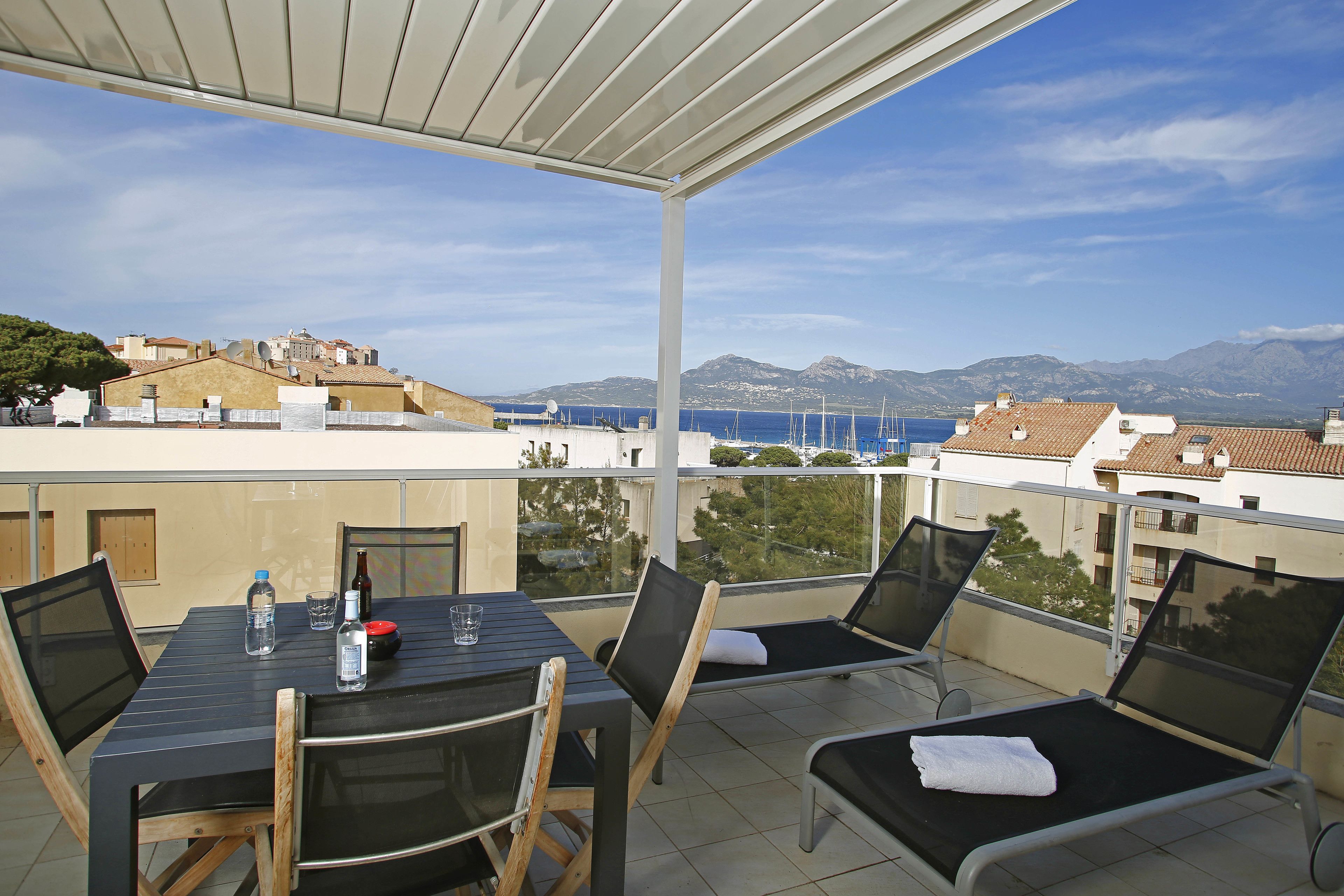 Un balcon avec une table, des chaises et une vue sur la mer et les montagnes.