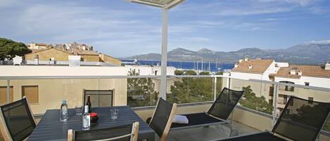 A balcony with a table, chairs, and a view of the sea and mountains.