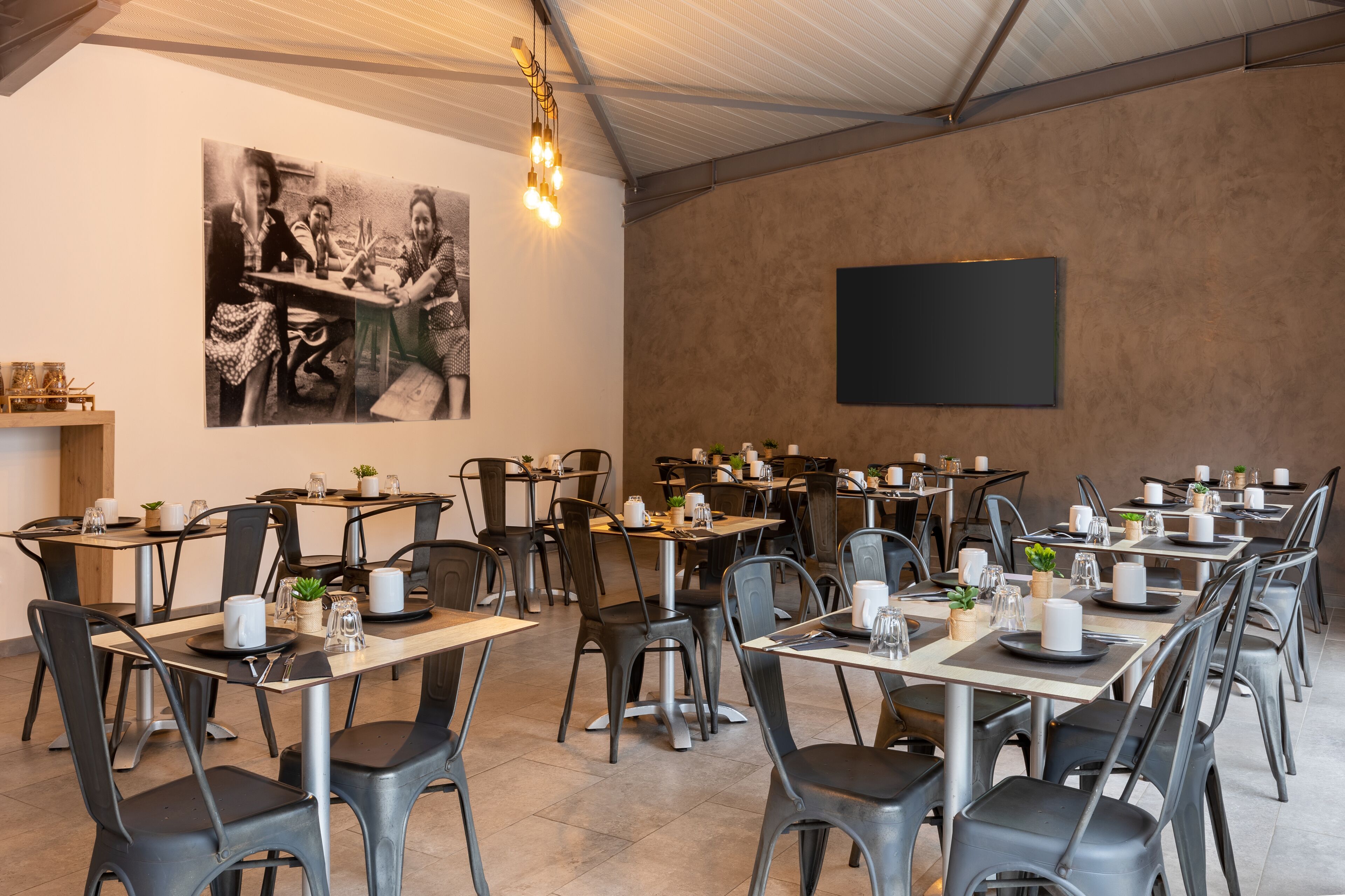 A dining area with multiple tables and chairs, a blackboard on the wall, and a hanging light fixture.