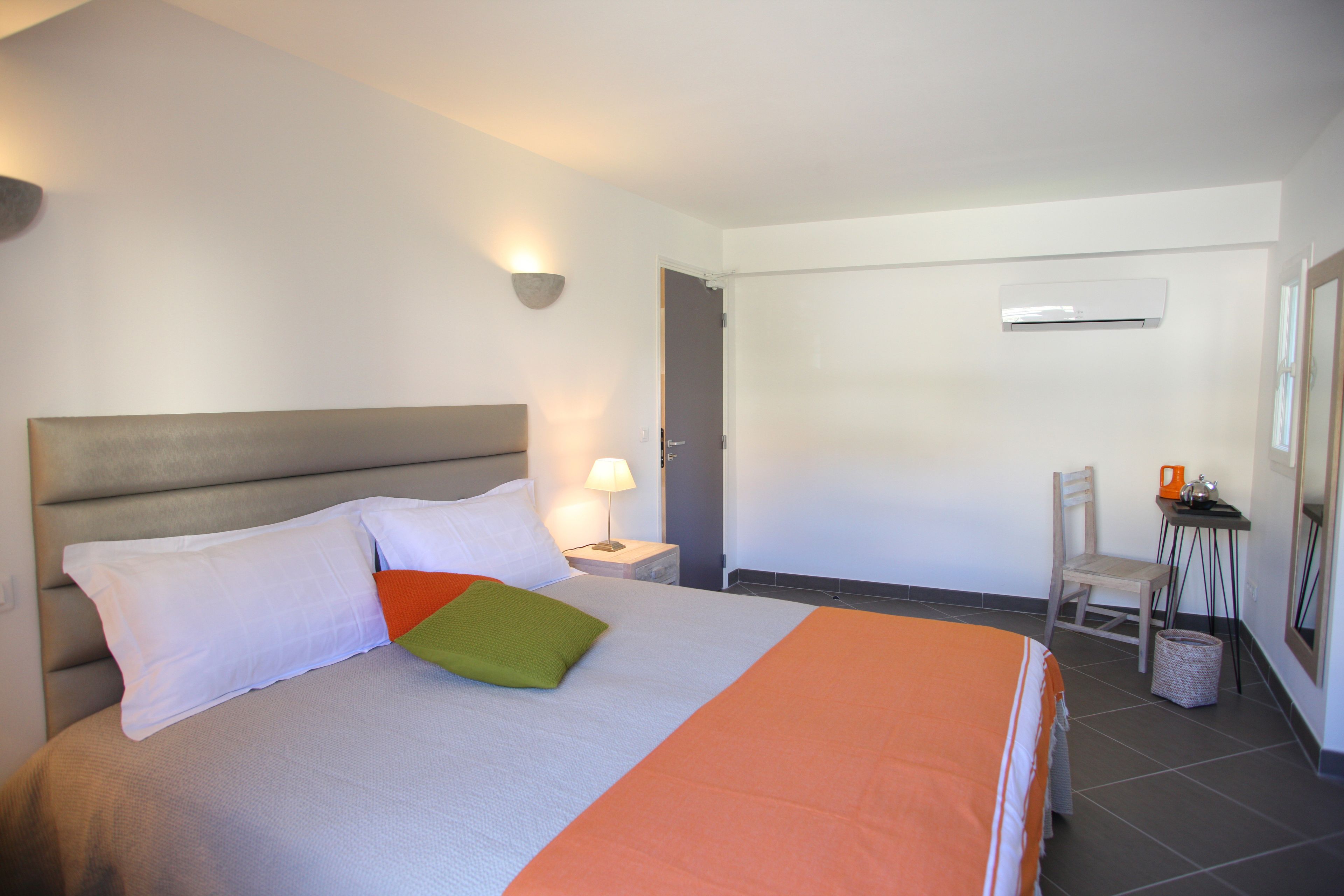 Een hotelkamer met een bed, nachtkastje, stoel, bureau en airconditioning.