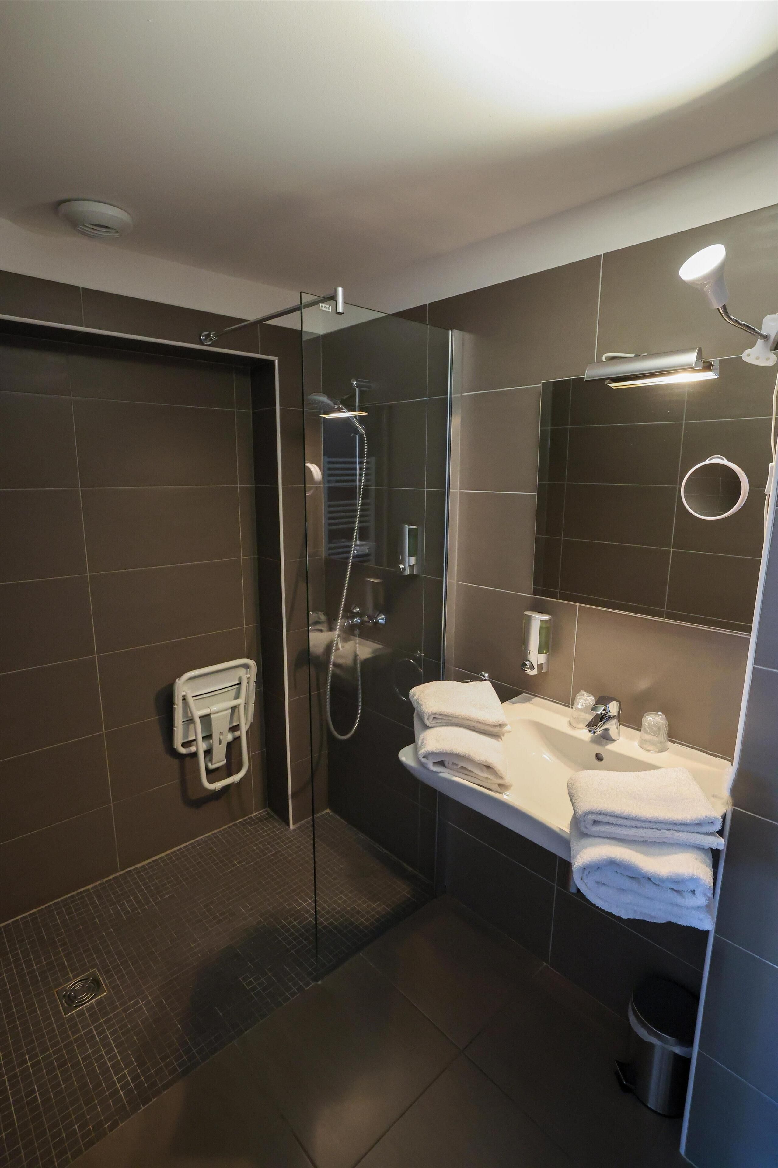 A modern bathroom with a glass-enclosed shower, a sink with a mirror, and a towel rack.
