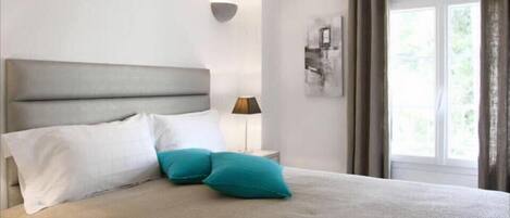 A neatly made bed with white and teal pillows, a grey headboard, and a bedside lamp.