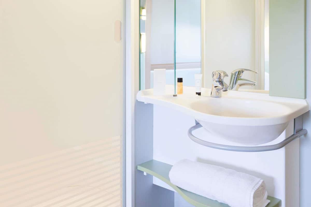 A bathroom with a white sink, a mirror, and a towel on a shelf.