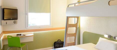 Una habitación de hotel con literas, un escritorio con silla, un televisor y una ventana.