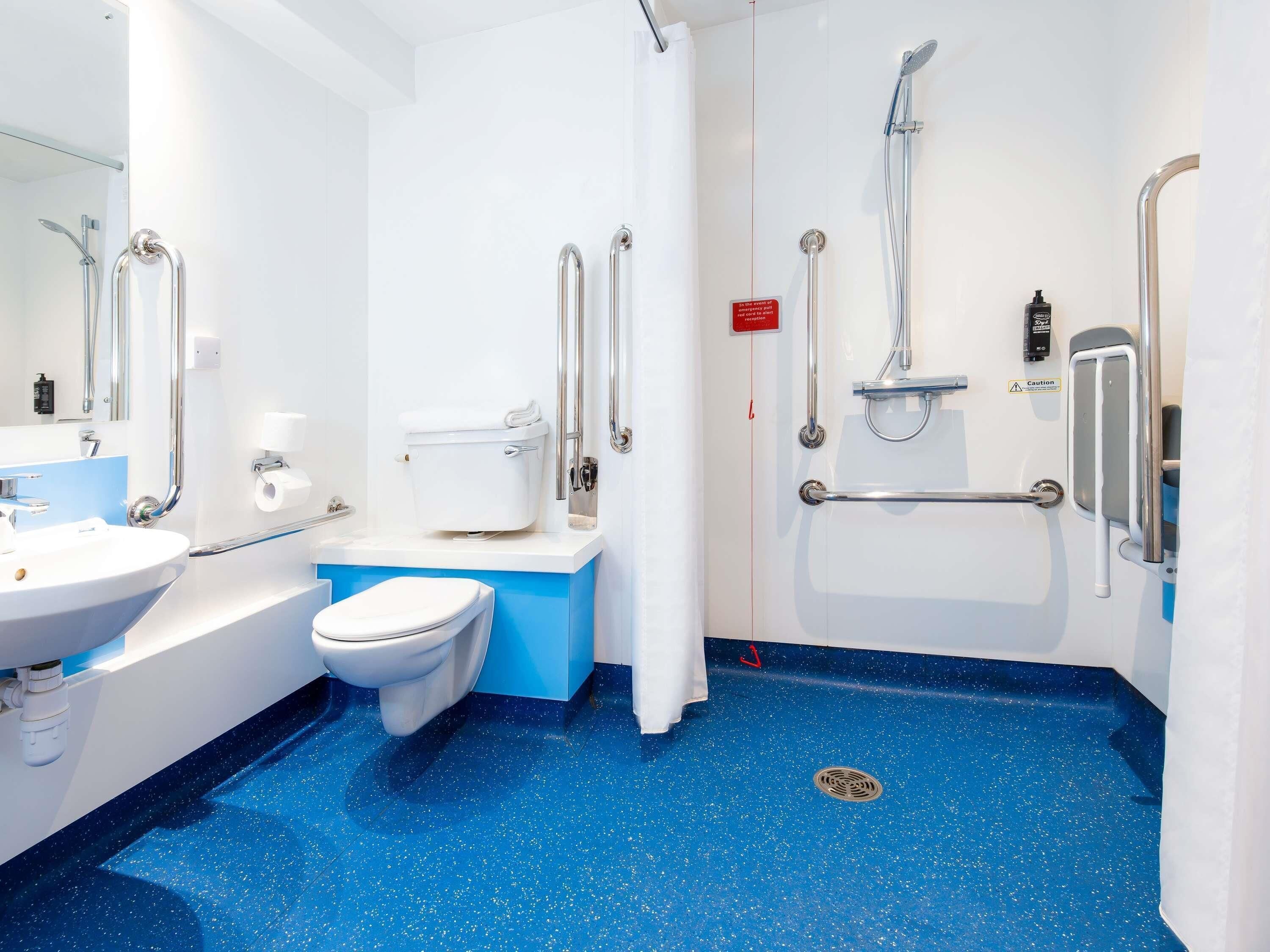 A bathroom with a white toilet, a sink, and a shower area with grab bars.