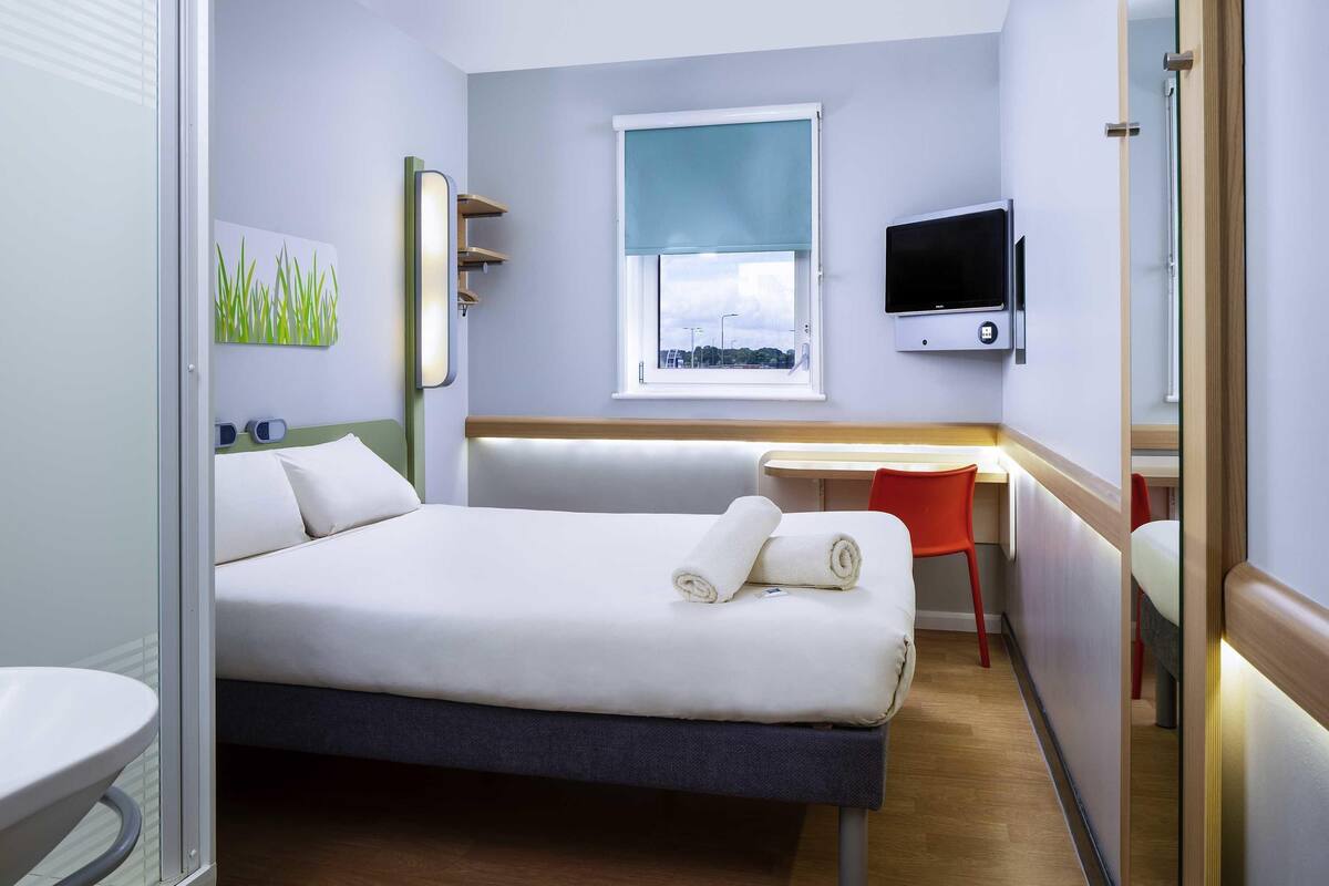 A hotel room with a bed, a desk, a chair, a TV, and a window with a view.