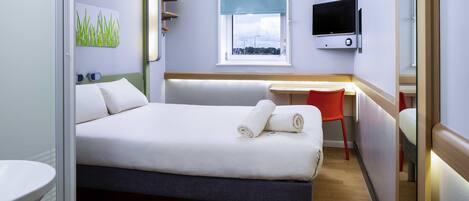 A hotel room with a bed, a desk, a chair, a TV, and a window with a view.