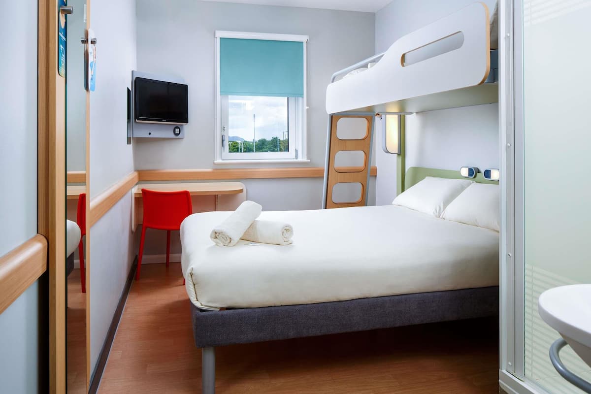 A bunk bed with a TV, a desk, a chair, and a window with a view.