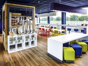 A modern cafe with a wooden counter, shelves with plates, and colorful seating. - ibis budget Edinburgh Park (Edinburgh)