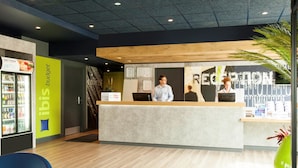 A reception area with a counter, a refrigerator with beverages, and a sign for 'hot pizza 24/7'. - ibis budget Edinburgh Park (Edinburgh)