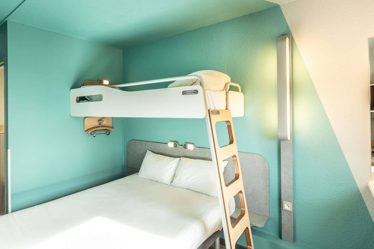 A bunk bed with a ladder, a bedside table, and a wall-mounted light fixture.