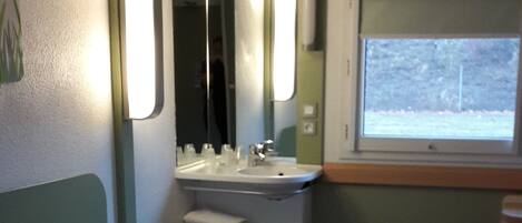 A hotel room with two beds, a sink, and a window.