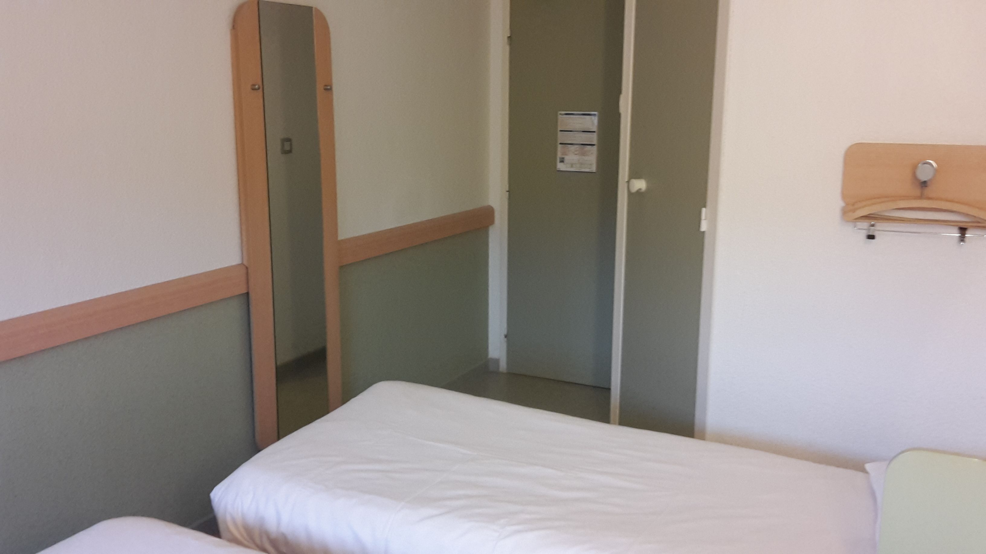 Een kleine, eenvoudige kamer met een enkel bed, een spiegel en een deur naar een andere kamer.