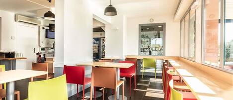 A modern restaurant interior with high tables, colorful chairs, and large windows.