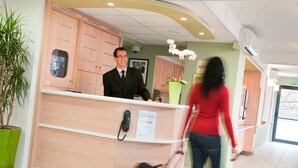 A hotel reception area with a wooden reception desk, a phone, and a sign indicating 'EN CAS DE ABSENCE' and 'DECOUPAGE'. - ibis budget Bourges (Le Subdray)