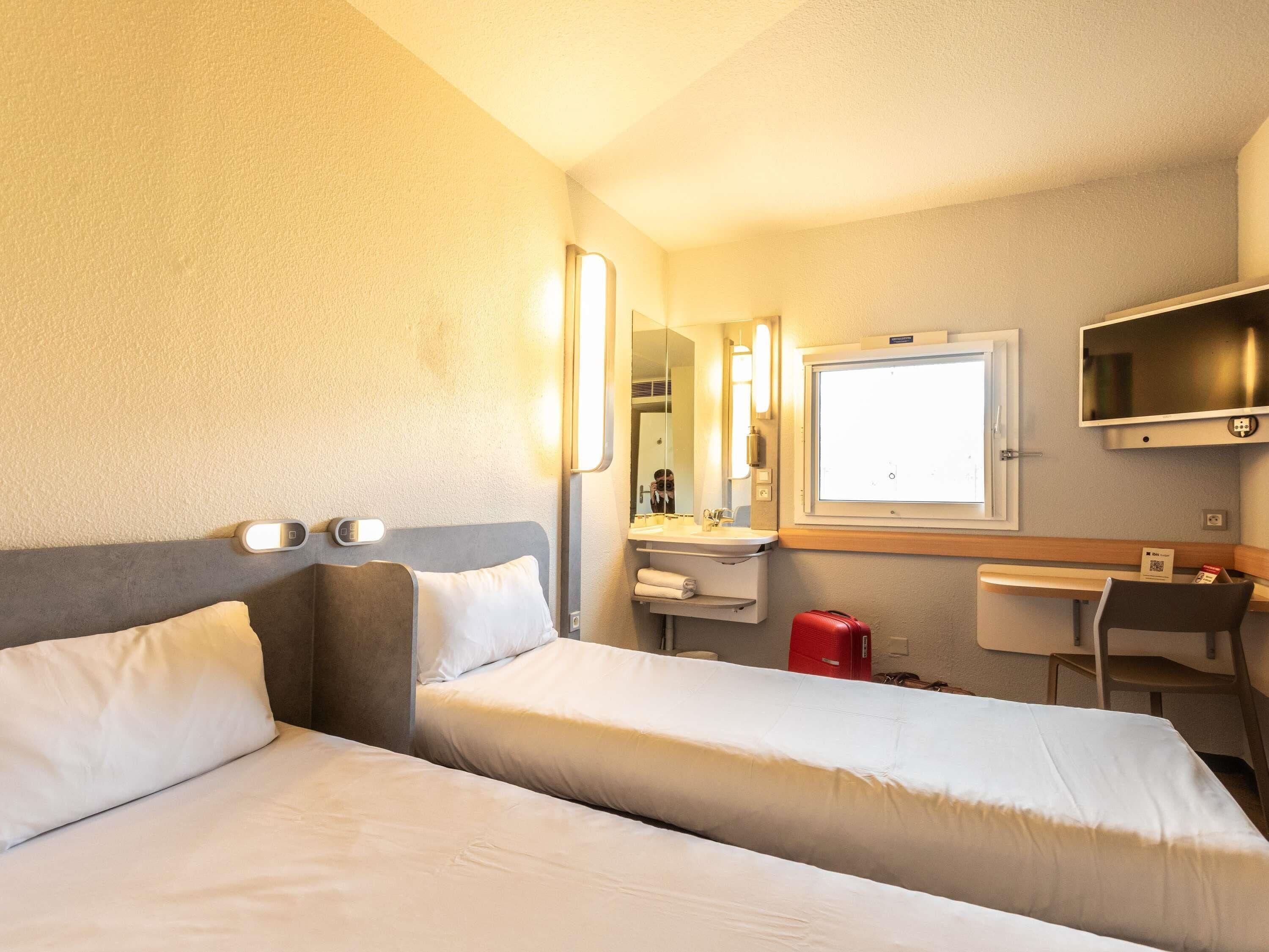 Een hotelkamer met twee bedden, een bureau, een televisie, een spiegel en een raam.