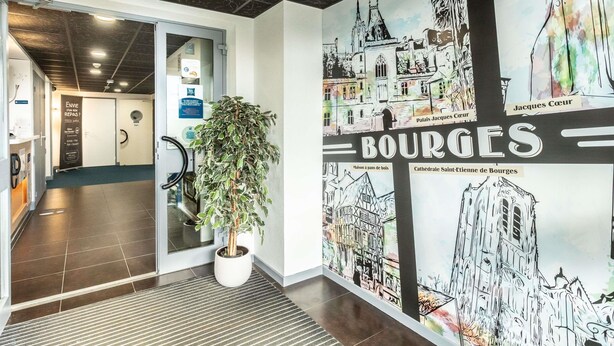 A hallway with a large wall mural of a cityscape, a potted plant, and a sign for a restaurant. - ibis budget Bourges (Le Subdray)