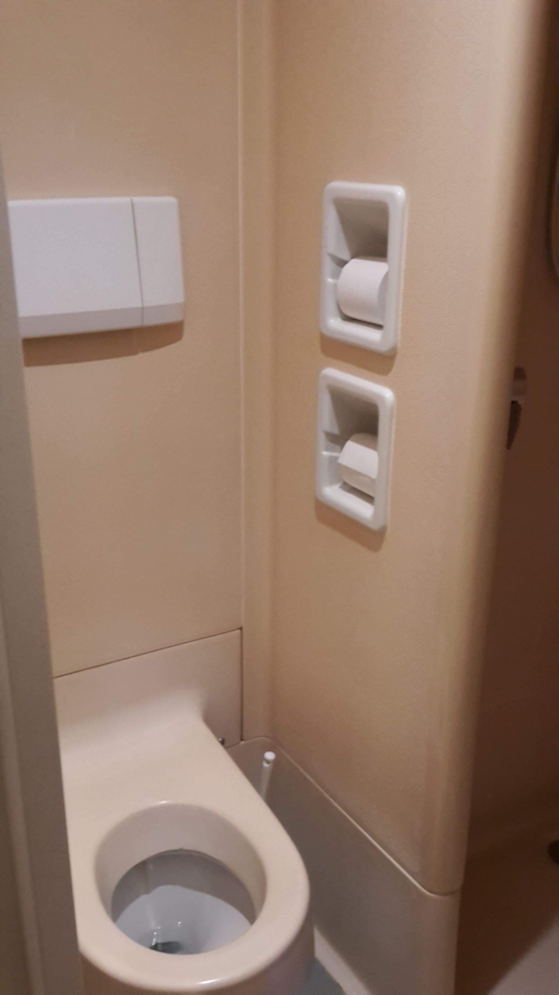 A small, narrow bathroom with a toilet, two paper towel dispensers on the wall, and a white cabinet above the toilet.