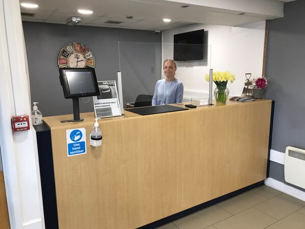 A reception desk with a clock, a sign offering half price parking, hand sanitizer, and a fire alarm.