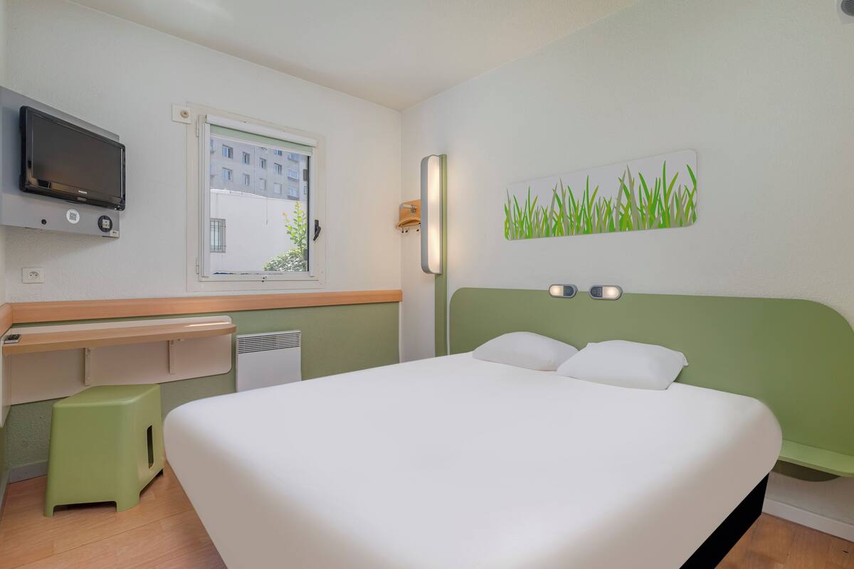 Une chambre d’hôtel équipée d’un lit, d’un bureau, d’une télévision, d’une fenêtre et d’une œuvre d’art murale.