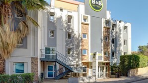 Un hôtel-restaurant de type « bed and breakfast » au design moderne, avec une enseigne bien visible, un escalier menant à l’entrée et une façade bien entretenue.