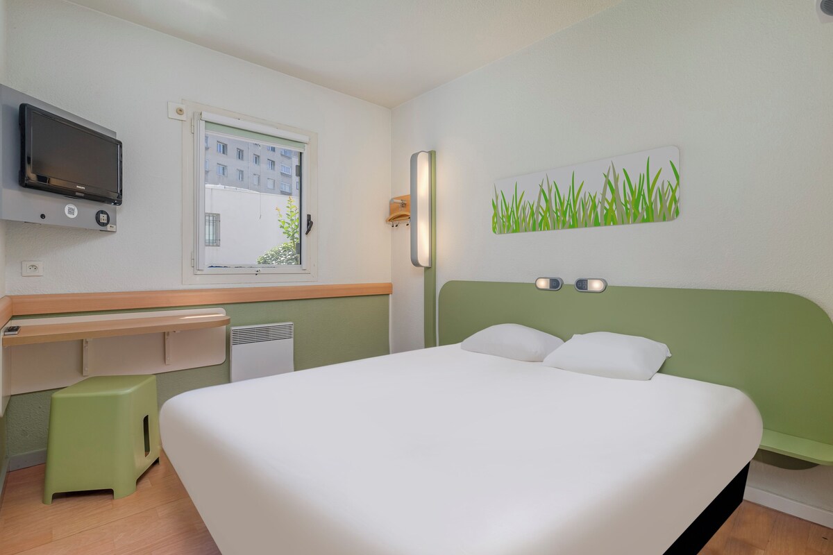 Une chambre d’hôtel équipée d’un lit, d’un bureau, d’une télévision, d’une fenêtre et d’une œuvre d’art murale.