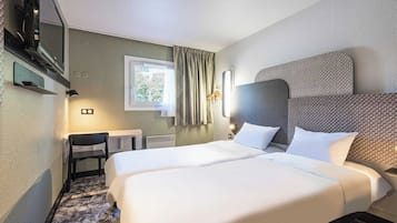 Camera d'albergo con due letti, una televisione, una sedia, una finestra con tende e una lampada a parete.
