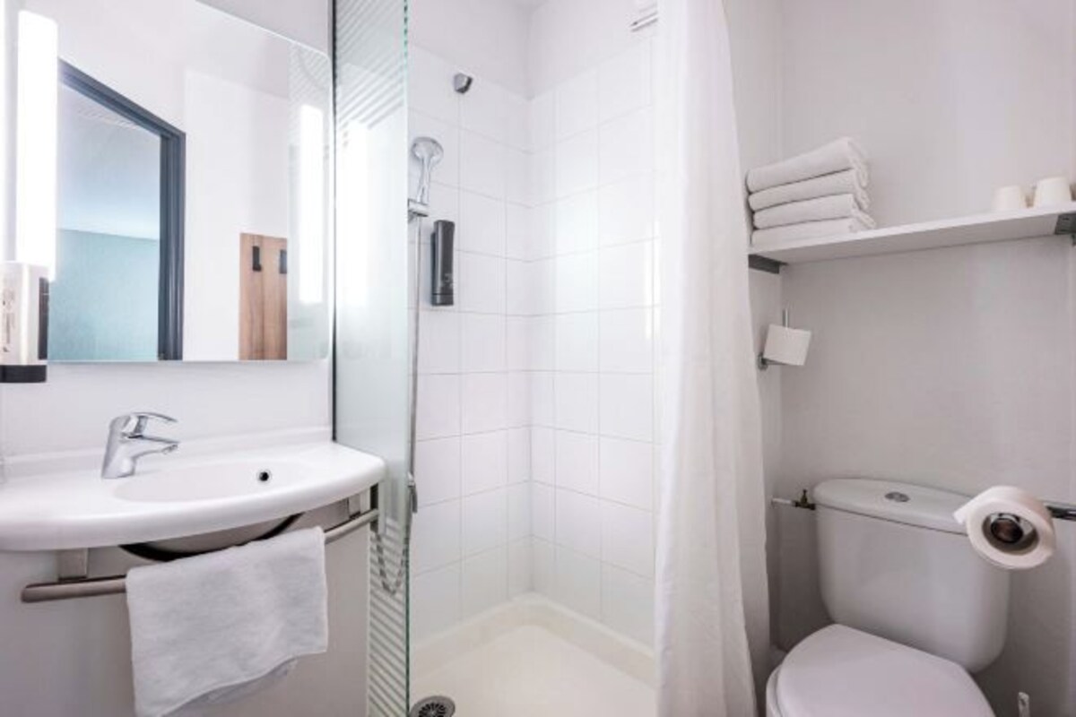 Un baño moderno con lavamanos, espejo, ducha, inodoro y toallero.