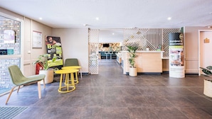 Un moderno hall de hotel con una recepción, un área de descanso y una escalera que lleva a los pisos superiores.