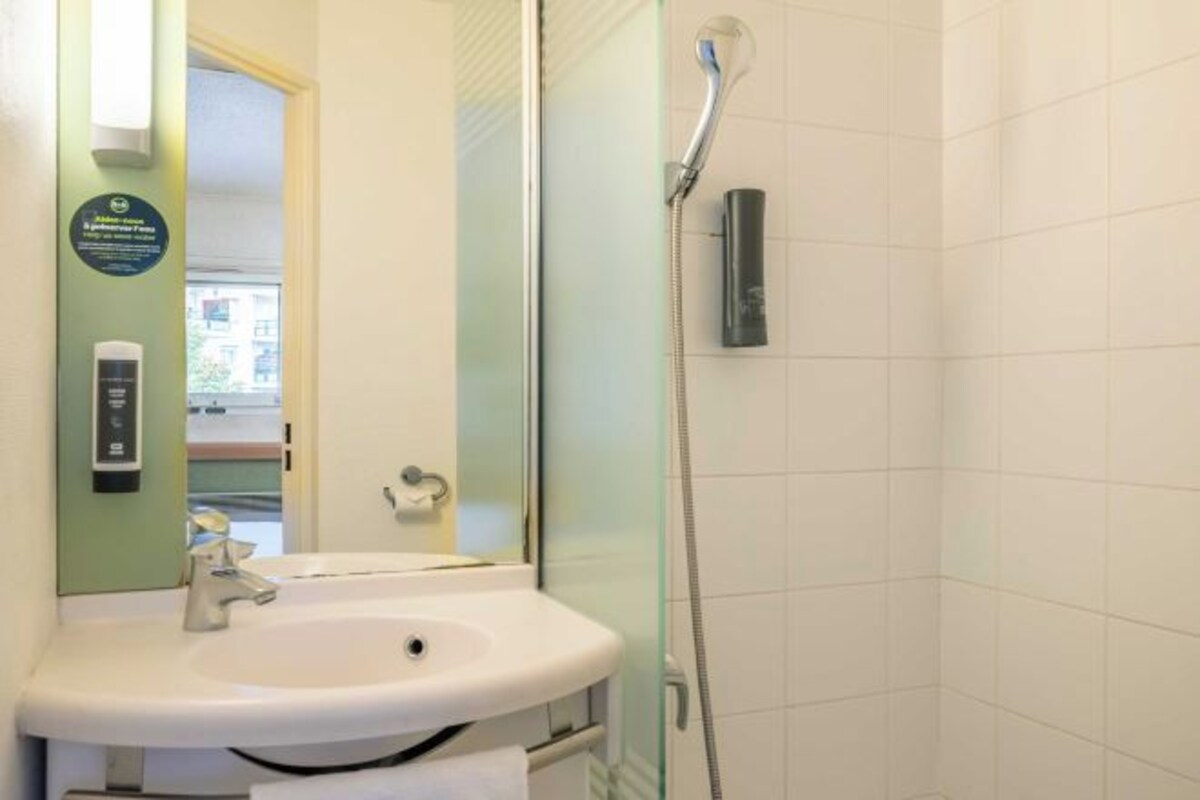 Un baño con un lavabo blanco, una cabina de ducha de vidrio y una toalla colgada en la pared.