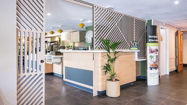 Zona de recepción de hotel con diseño moderno, que incluye un mostrador de recepción, un reloj y una planta en maceta.